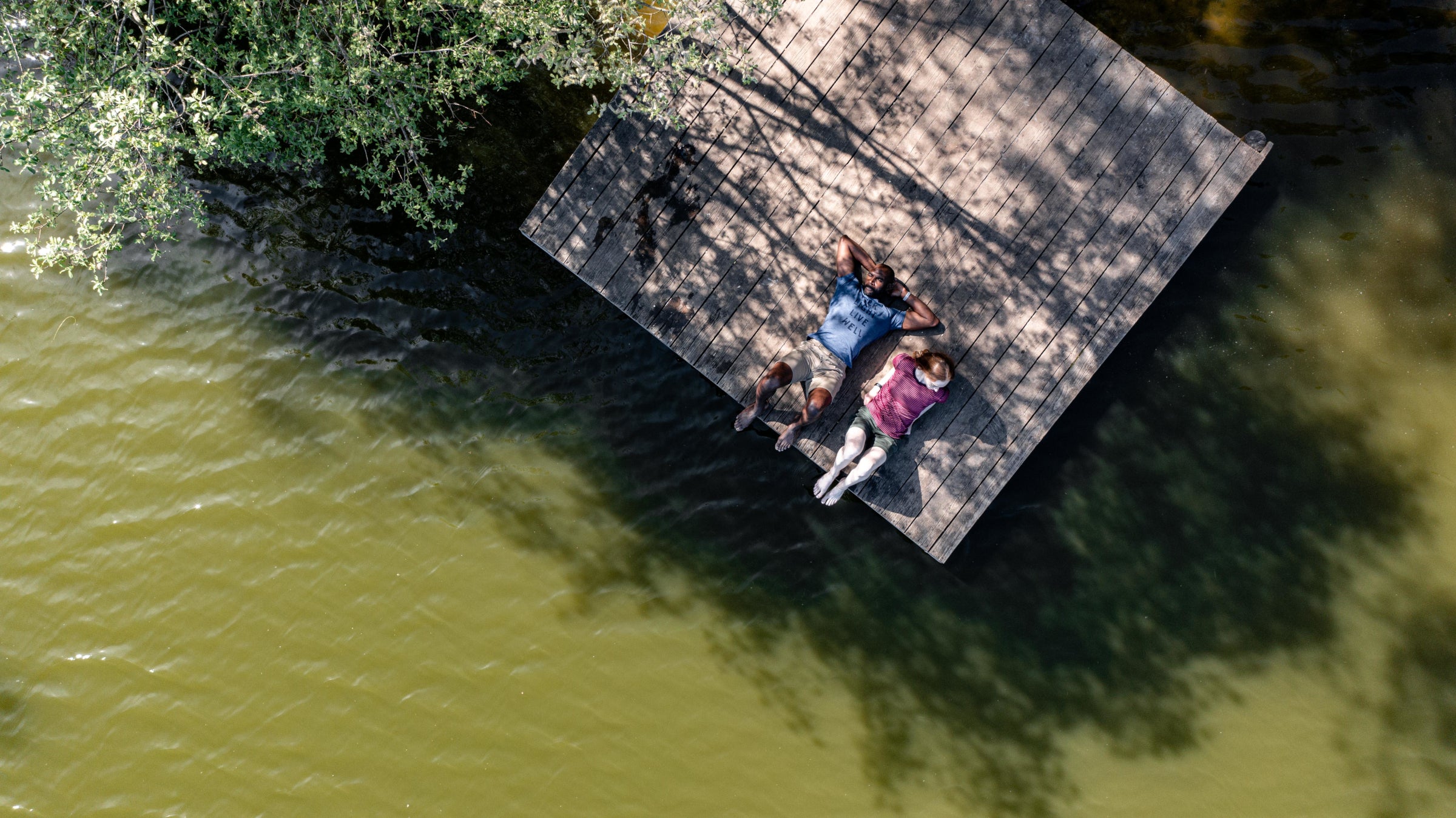 Two people are relaxing on a wooden dock over a lake, wearing Isobaa merino clothing