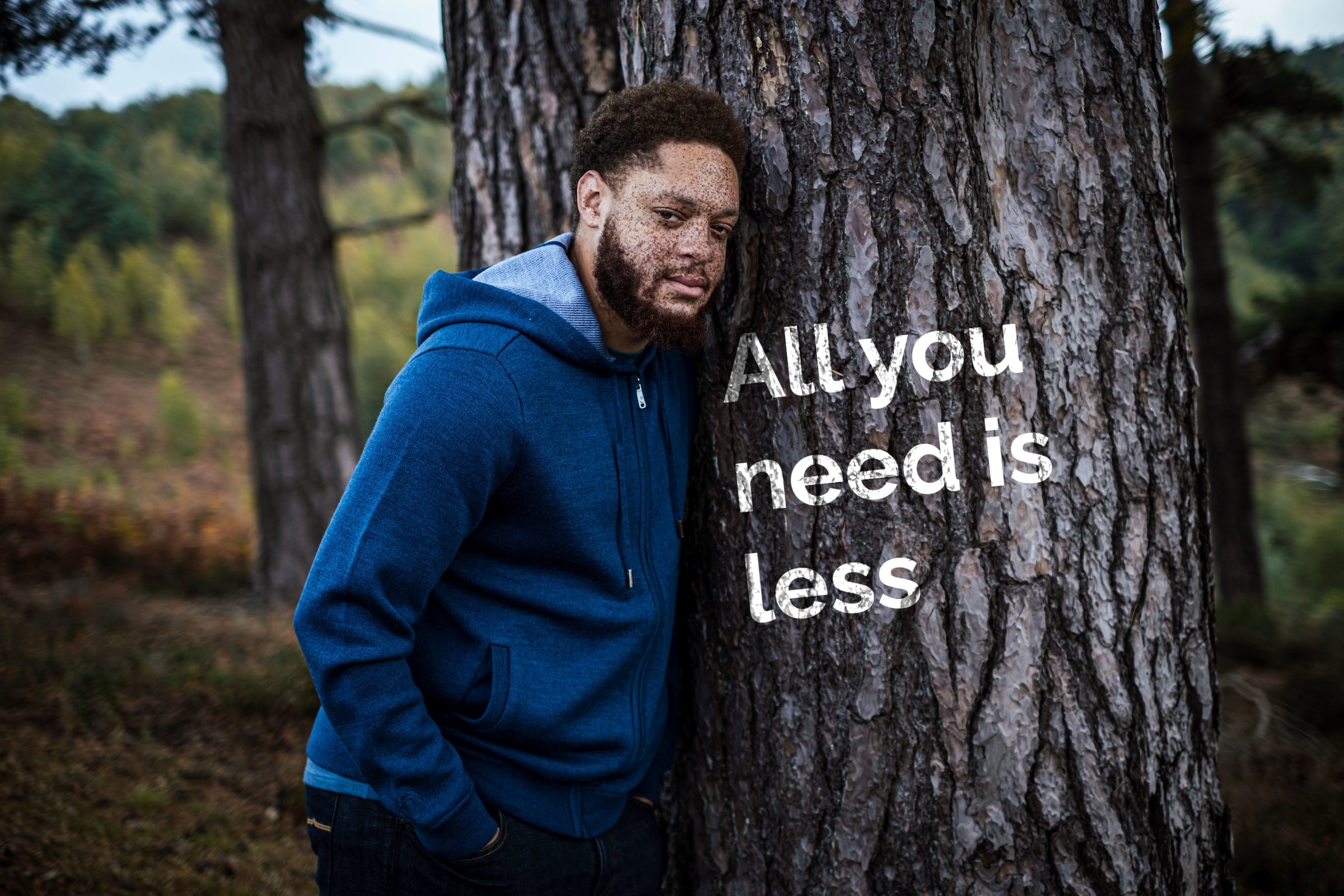 Man in a petrol Isobaa Lux Hoodie leaning against a tree