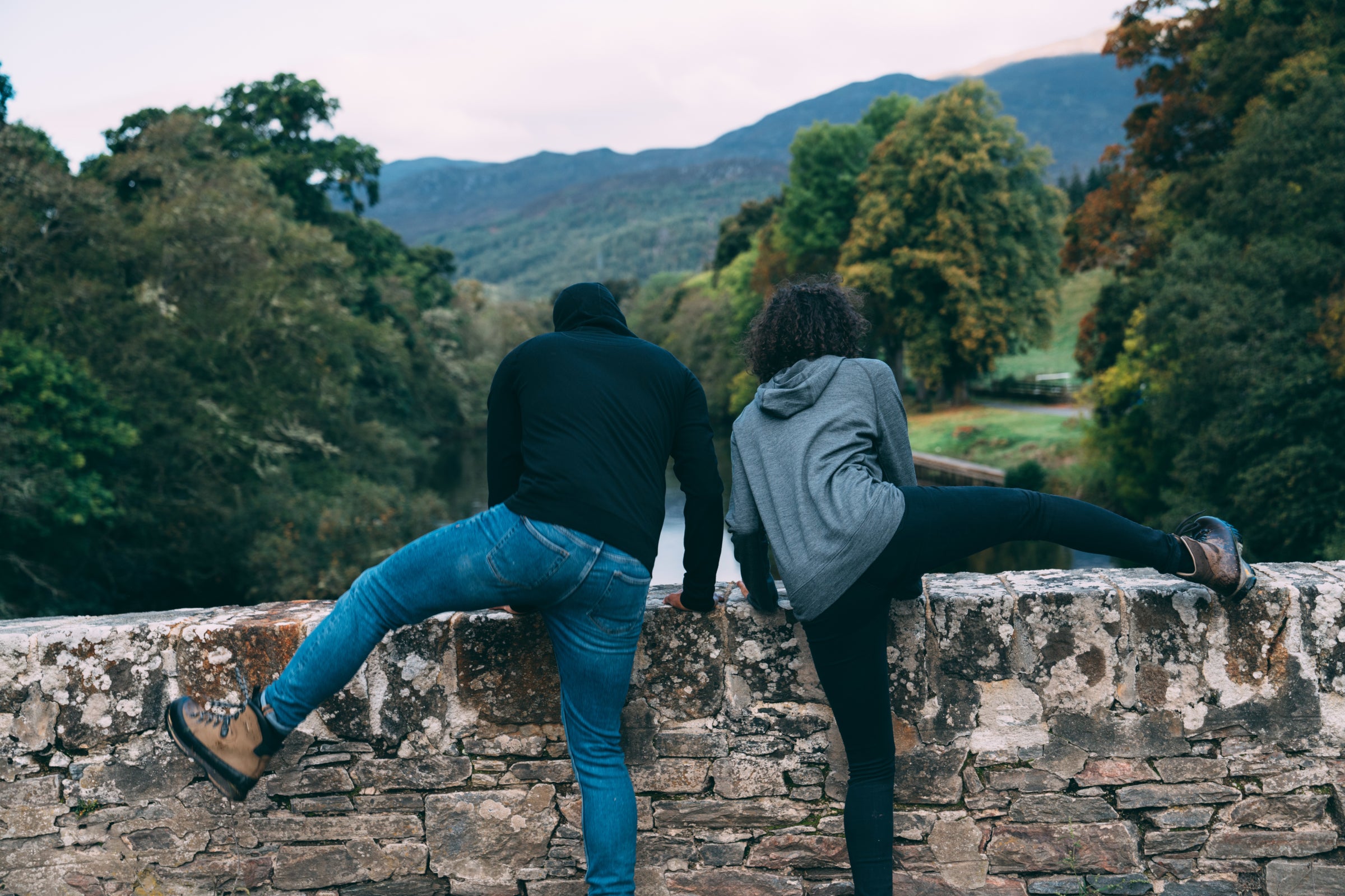 Two people climbing on a wall overlooking a scenic valley with autumn colours