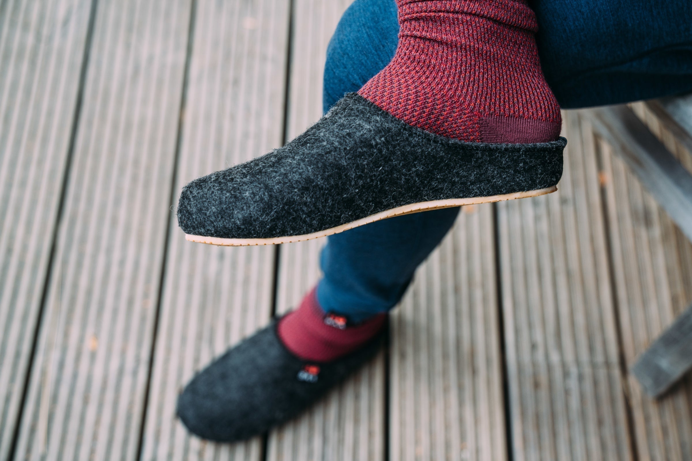 Close-up of dark grey merino blend slippers paired with red socks, sitting on a wooden deck