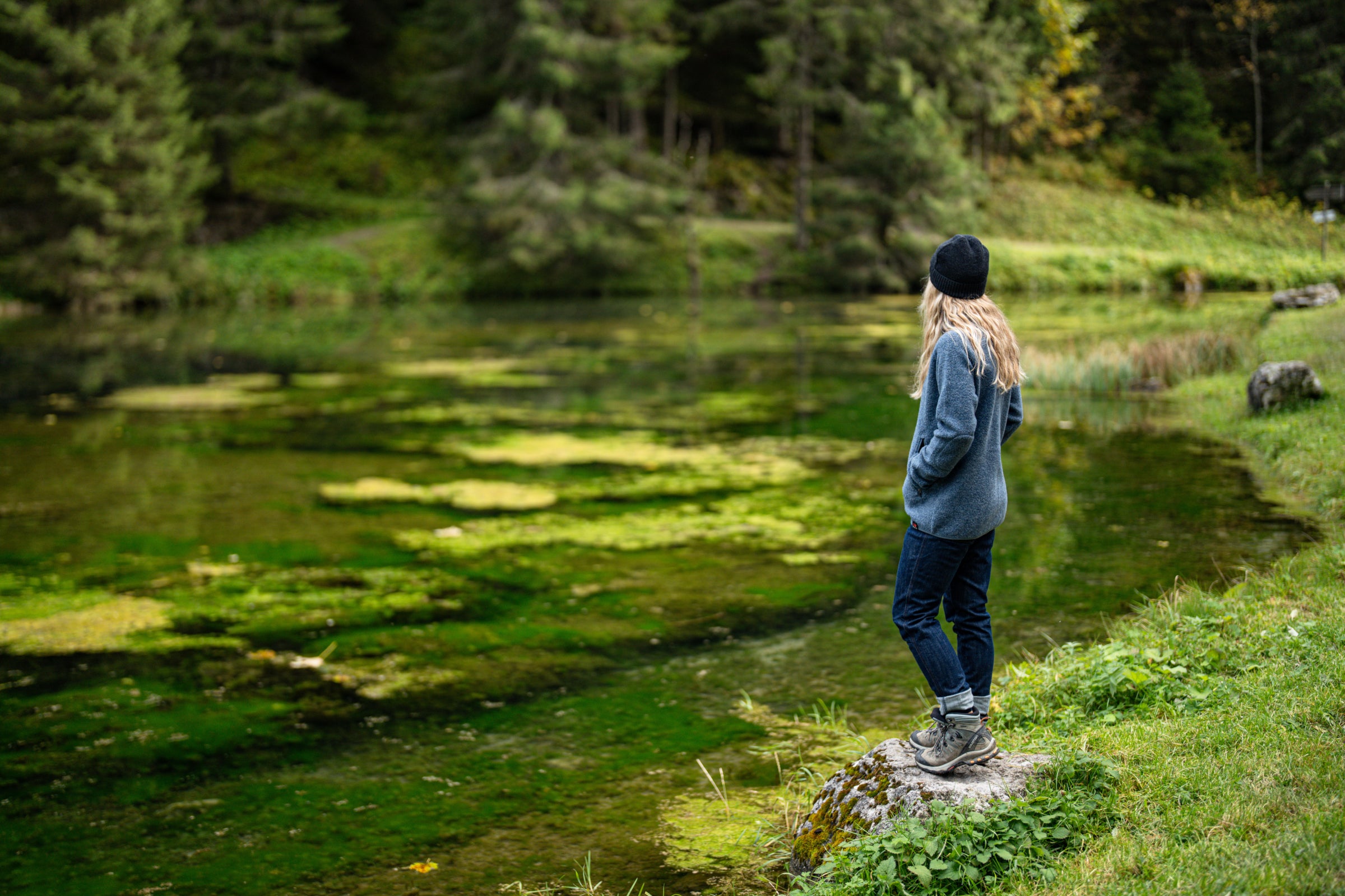 Person standing by a lush green pond in the outdoors