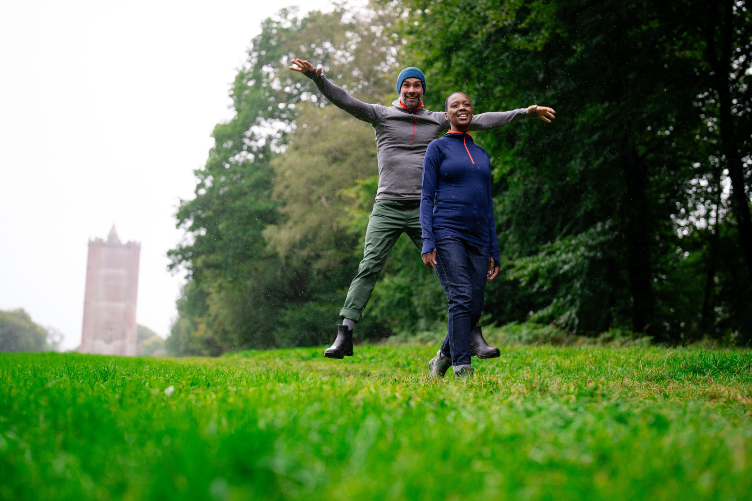 A man and a woman outdoors, with the man jumping joyfully in the background