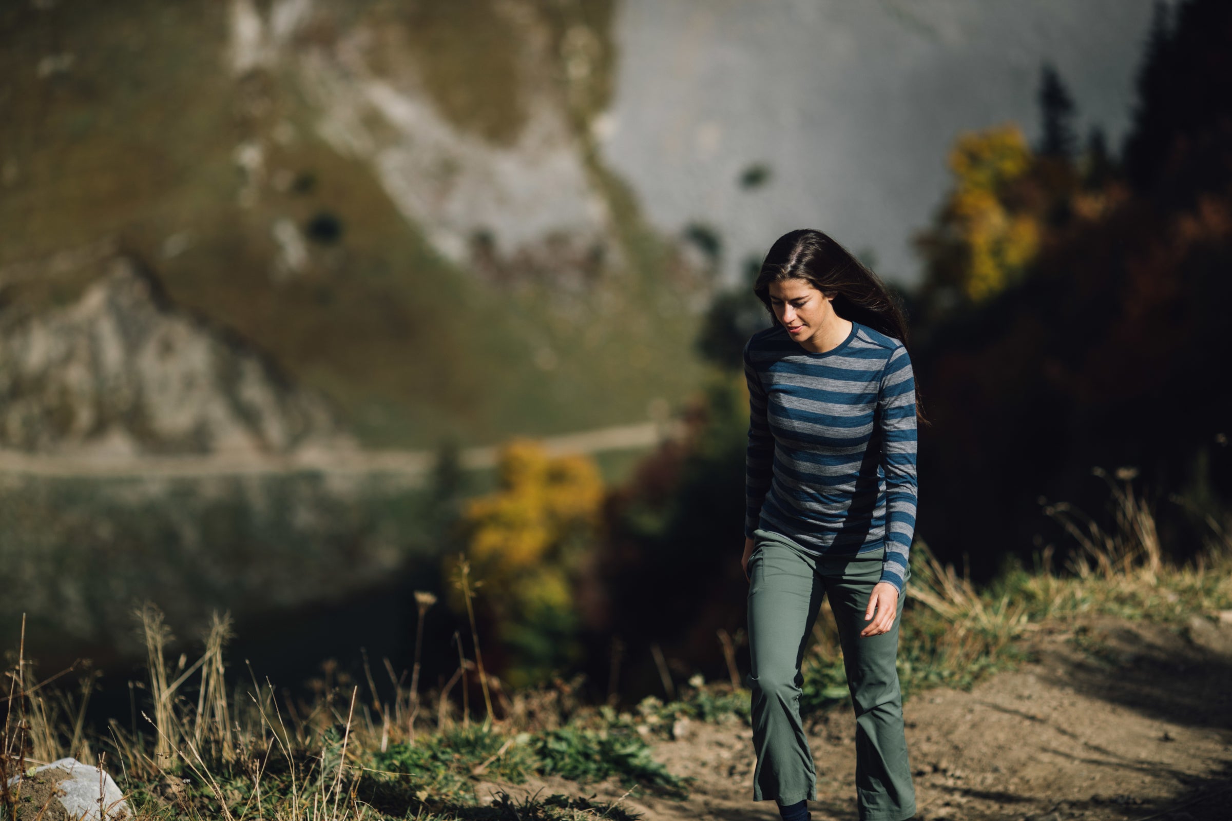 A woman hiking uphill on a trail wearing a striped Merino wool top