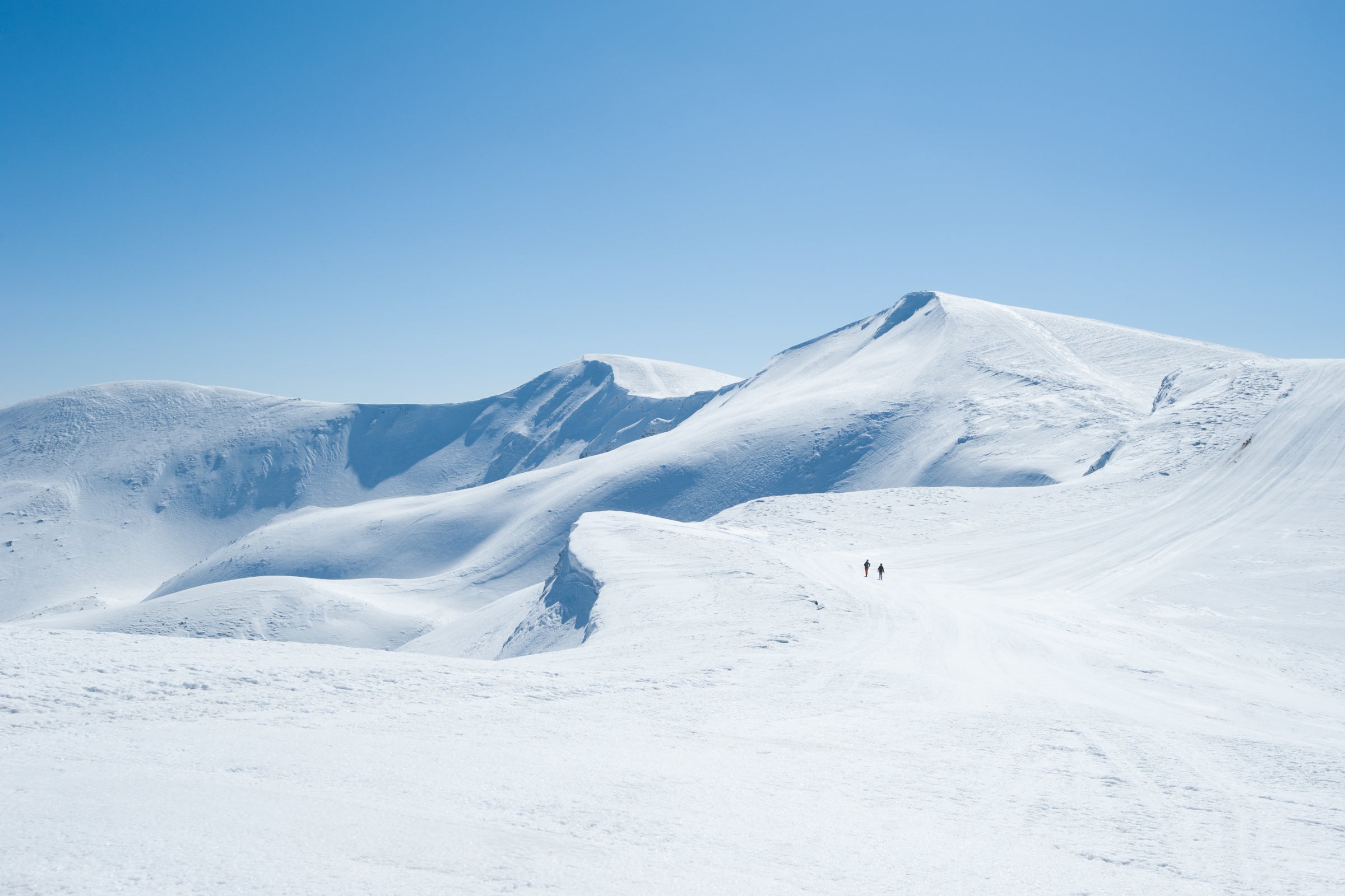 Snowy mountain landscape with two distant hikers