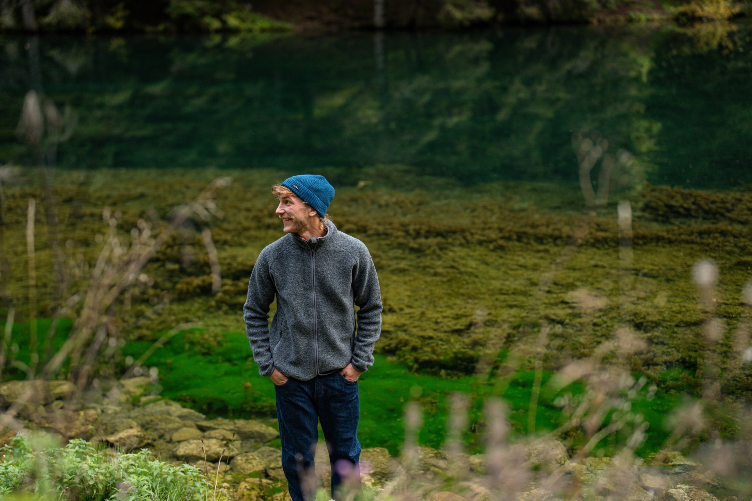 A man in a merino fleece by a clear green pond