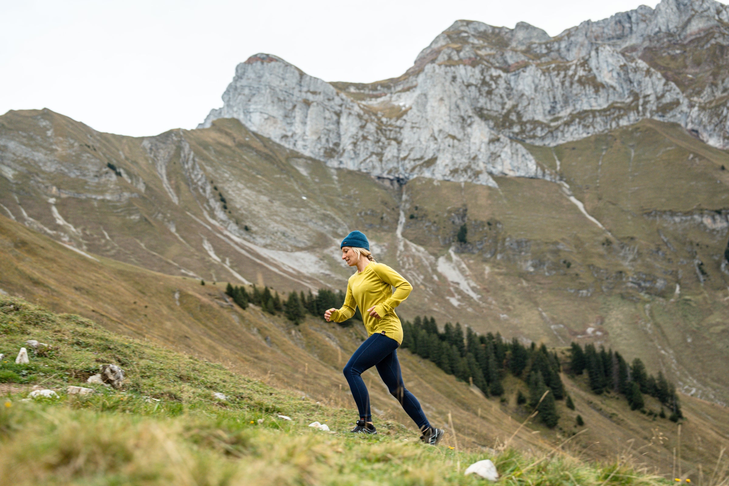 Woman running uphill in Isobaa merino activewear, surrounded by mountains