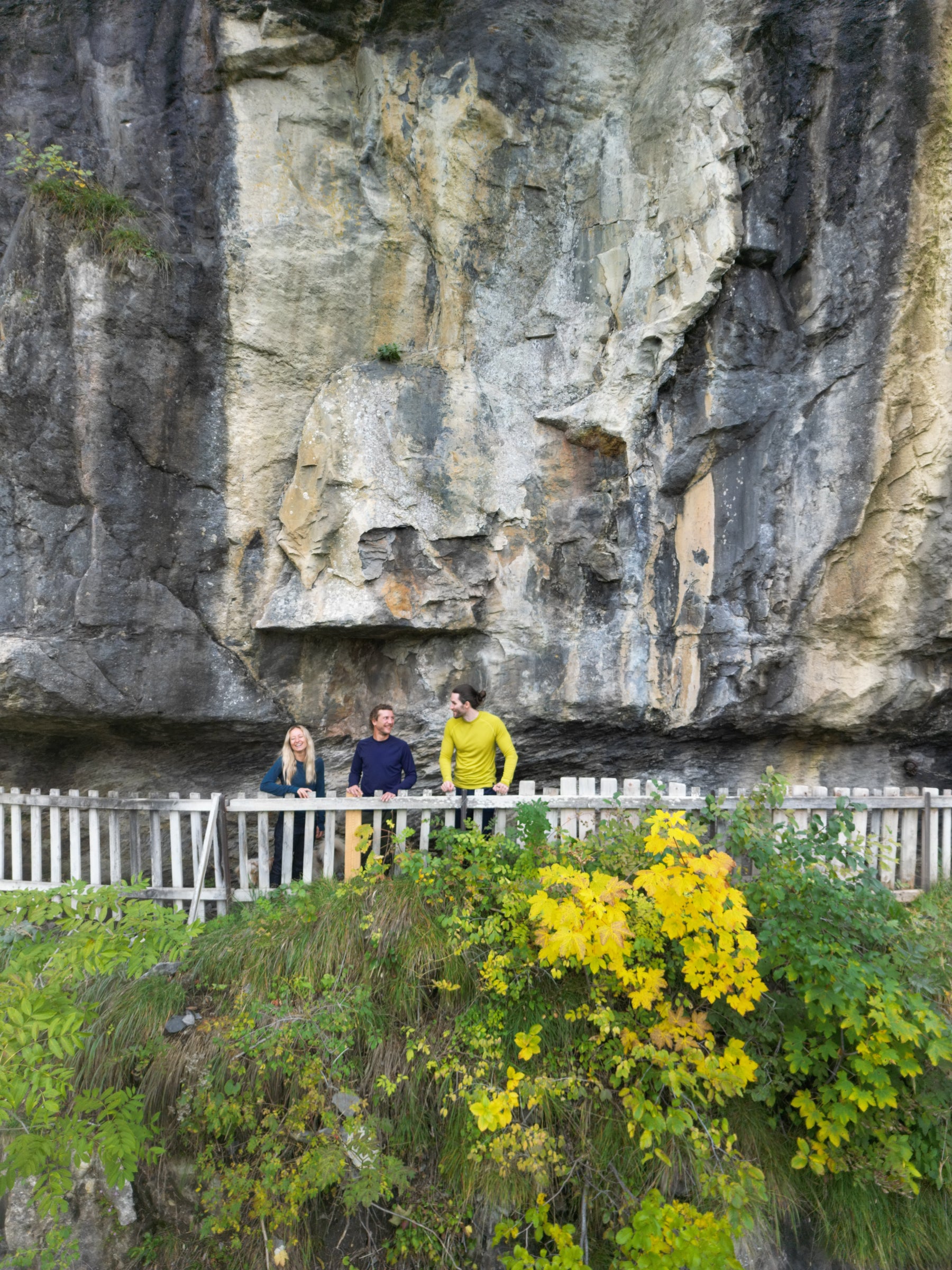 Three people chatting on a wooden walkway by a rocky cliff