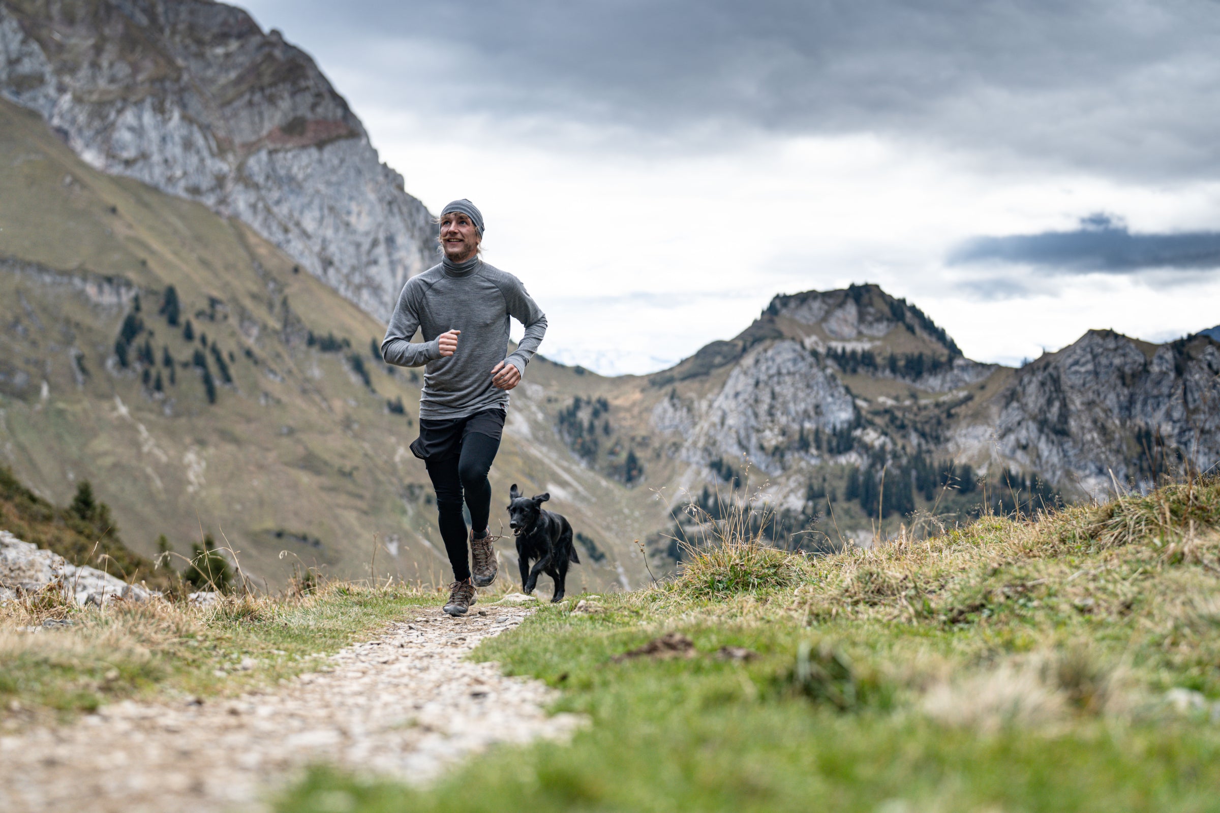 Man trail running in the mountains with a dog, in Isobaa merino