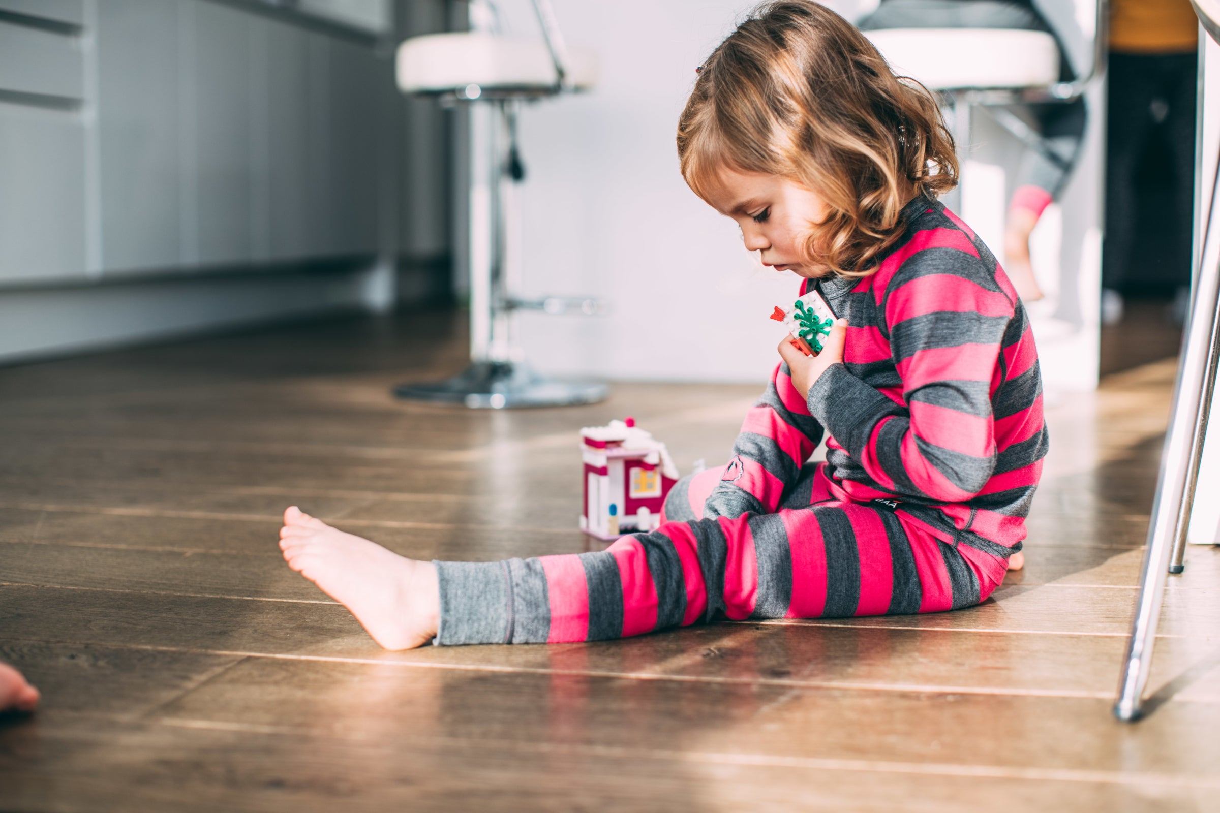 A young girl playing with toys indoors, dressed in a pink and grey striped Isobaa Merino Blend 200 Long Sleeve Crew and Merino Blend 200 Leggings