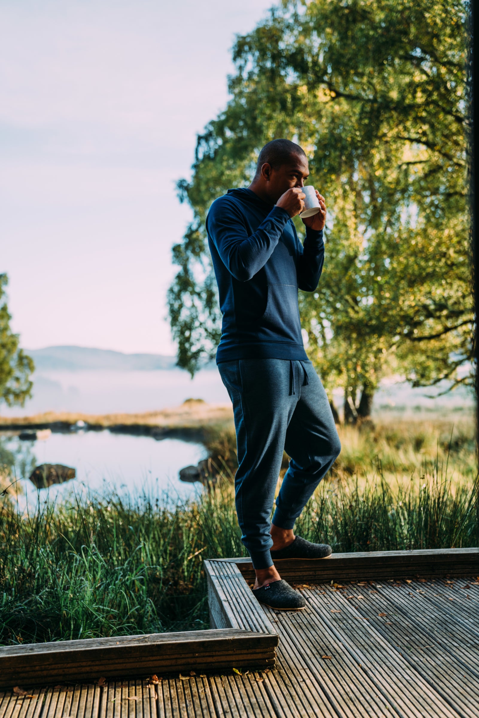 Man enjoying a cup of coffee outdoors, wearing dark grey merino blend slippers and navy loungewear