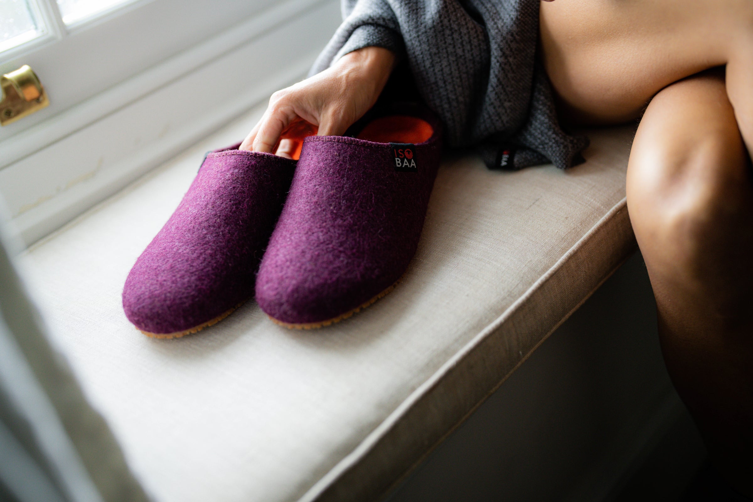 Purple merino blend slippers with an orange lining, resting on a window seat