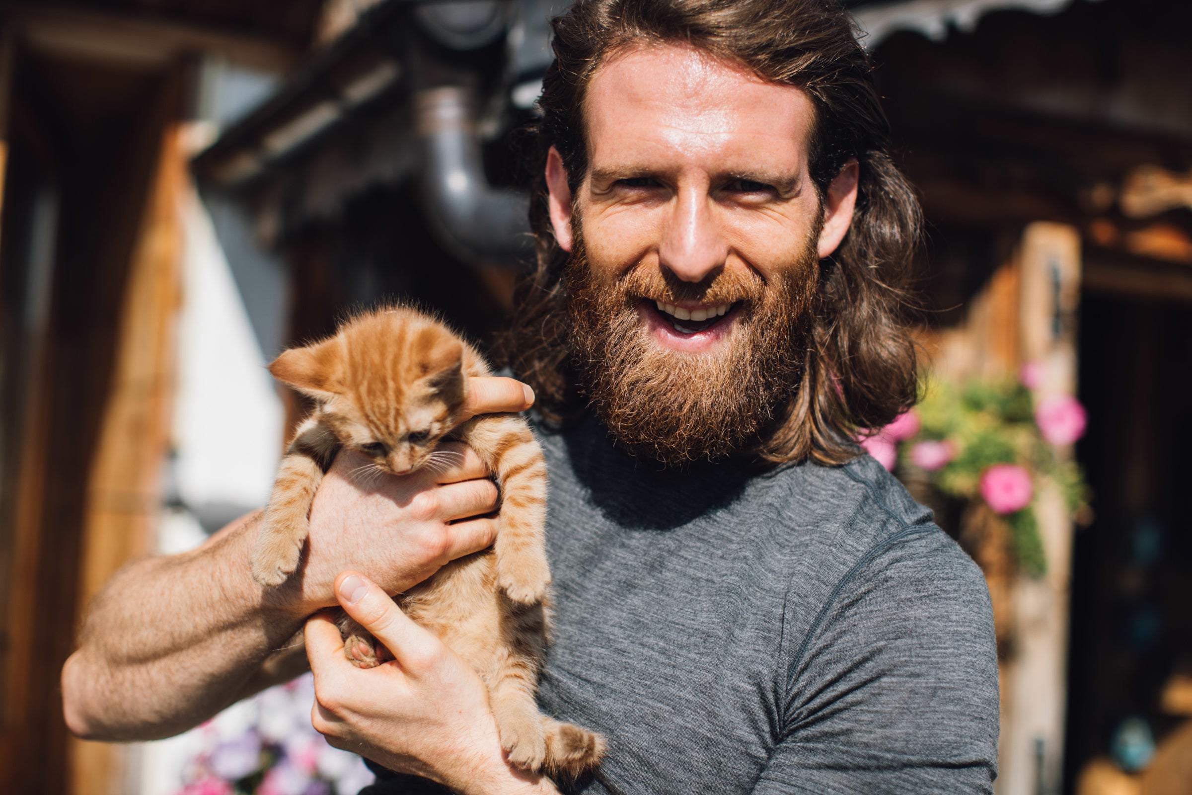 A man with long hair and a beard holding a small orange kitten outdoors