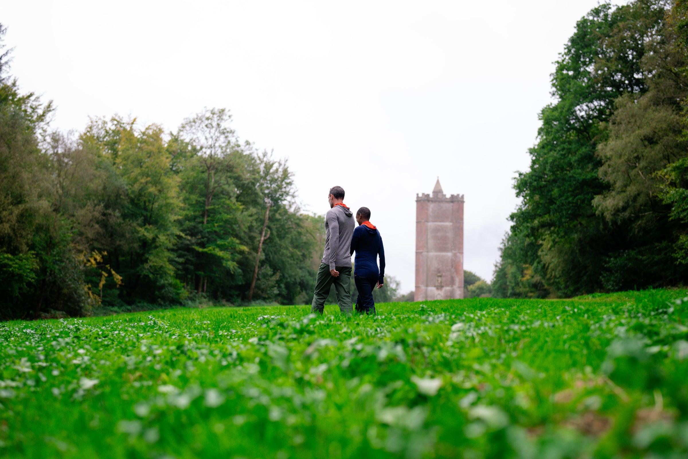 Two people walking through a lush green field with a tall tower in the background